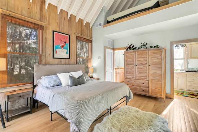 bedroom with ensuite bath, light hardwood / wood-style flooring, beamed ceiling, high vaulted ceiling, and wooden walls