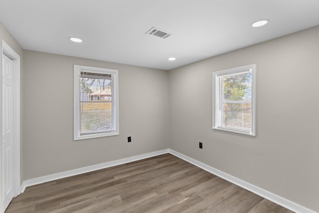 spare room with a wealth of natural light, recessed lighting, baseboards, and wood finished floors