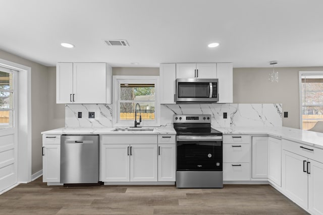 kitchen featuring stainless steel appliances, a sink, visible vents, white cabinets, and hanging light fixtures