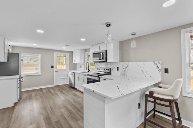 kitchen featuring pendant lighting, stainless steel appliances, decorative backsplash, white cabinets, and a peninsula