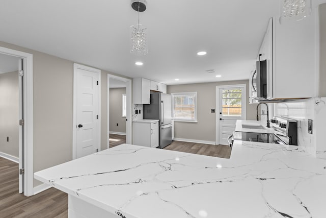 kitchen featuring dark wood finished floors, stainless steel appliances, hanging light fixtures, white cabinets, and a peninsula