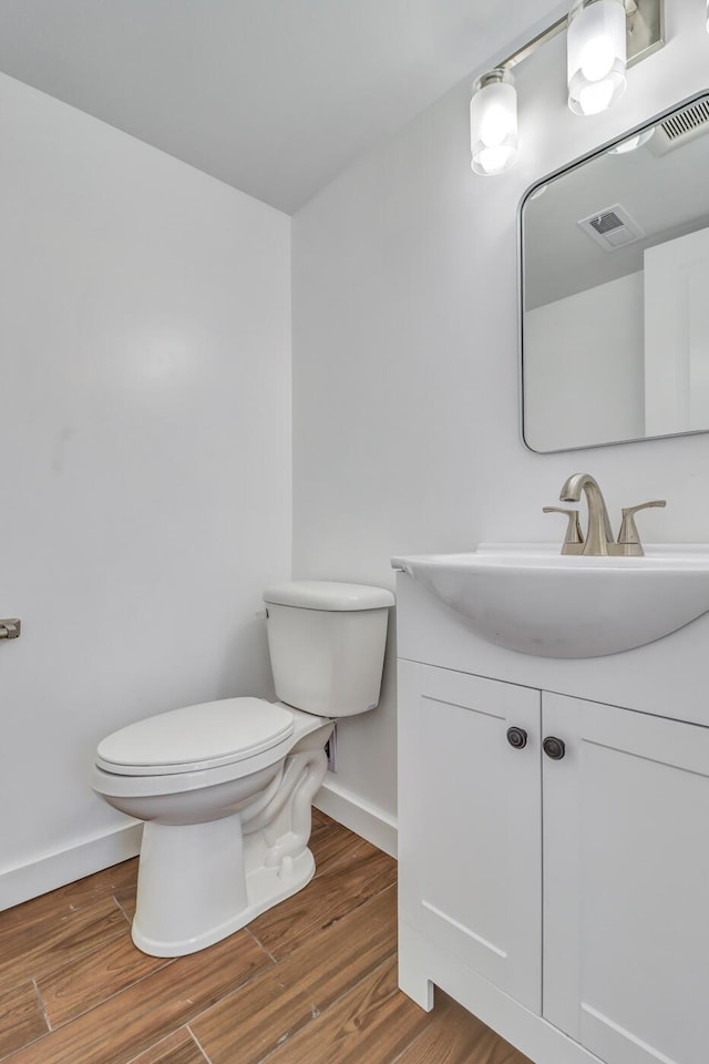 half bath featuring visible vents, baseboards, toilet, wood finished floors, and vanity