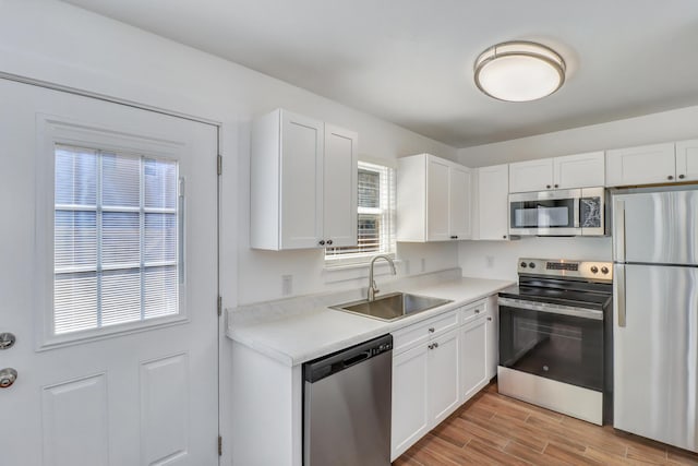 kitchen featuring appliances with stainless steel finishes, white cabinetry, wood tiled floor, and a sink