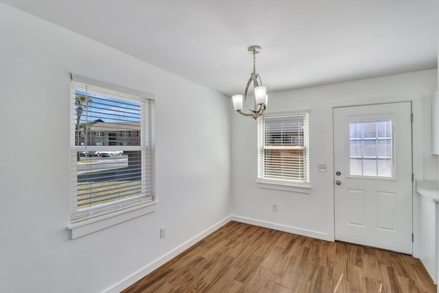 unfurnished dining area featuring plenty of natural light, an inviting chandelier, baseboards, and wood finished floors