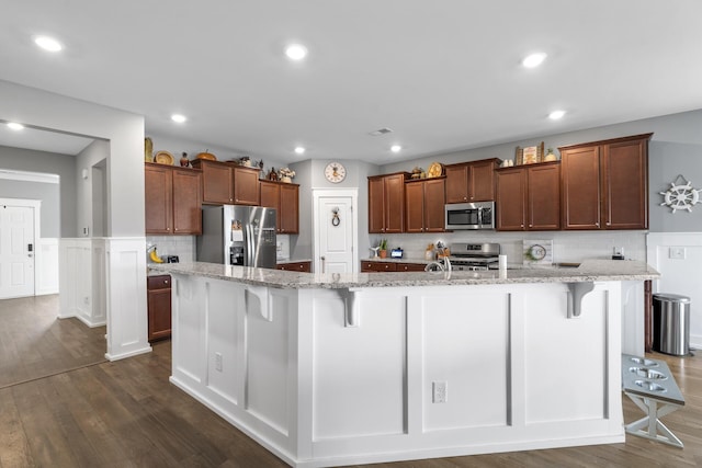 kitchen featuring a kitchen bar, a large island with sink, dark hardwood / wood-style flooring, and stainless steel appliances