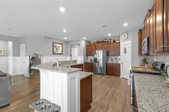 kitchen featuring stainless steel appliances, light stone counters, backsplash, hardwood / wood-style floors, and a center island with sink