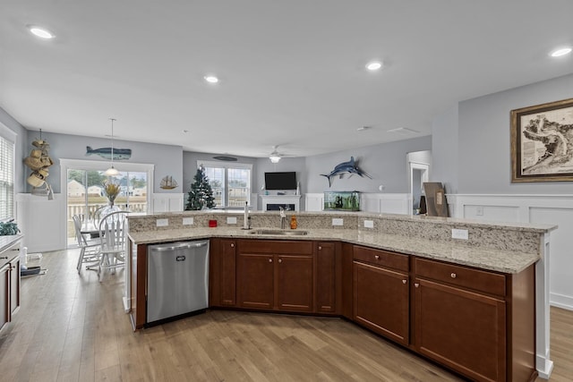 kitchen with ceiling fan, dishwasher, hanging light fixtures, light hardwood / wood-style flooring, and a center island with sink