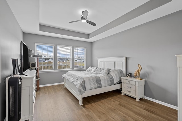 bedroom with hardwood / wood-style floors, ceiling fan, and a raised ceiling