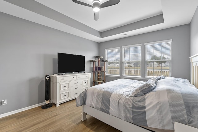 bedroom featuring a raised ceiling, ceiling fan, and light wood-type flooring