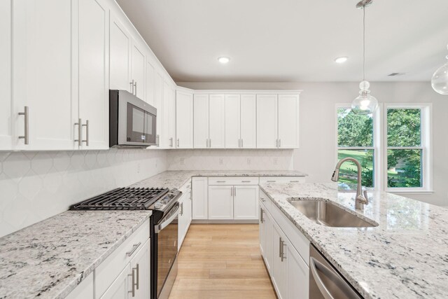 kitchen featuring sink, pendant lighting, light wood-type flooring, appliances with stainless steel finishes, and white cabinetry