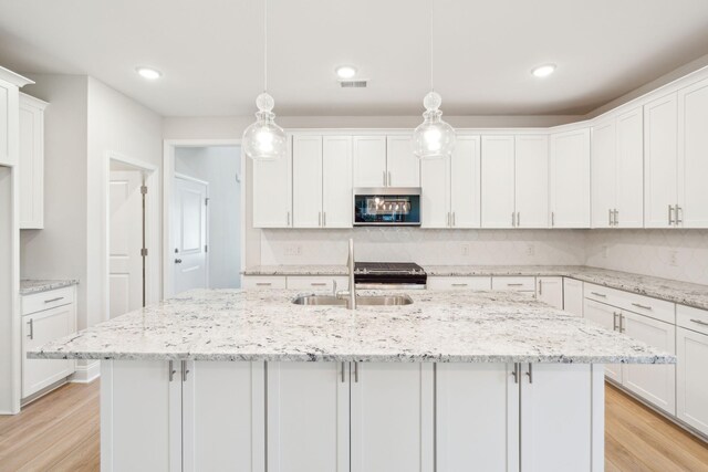 kitchen with light wood-type flooring, white cabinetry, decorative light fixtures, and appliances with stainless steel finishes