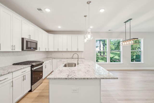 kitchen with light hardwood / wood-style floors, stainless steel appliances, sink, a kitchen island with sink, and pendant lighting