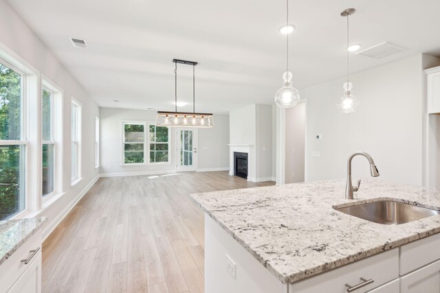 kitchen with light hardwood / wood-style floors, white cabinetry, sink, light stone countertops, and a kitchen island with sink