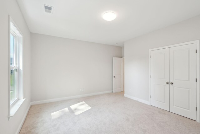 unfurnished bedroom with light colored carpet and a closet