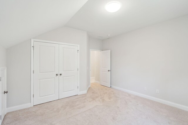 unfurnished bedroom featuring a closet, vaulted ceiling, and light colored carpet