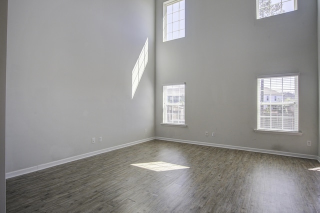 unfurnished room featuring a towering ceiling, dark wood-style floors, baseboards, and a wealth of natural light