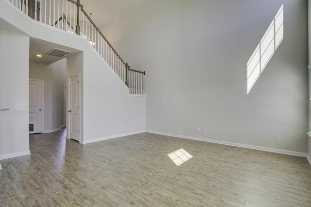 unfurnished living room with visible vents, baseboards, wood finished floors, and a towering ceiling