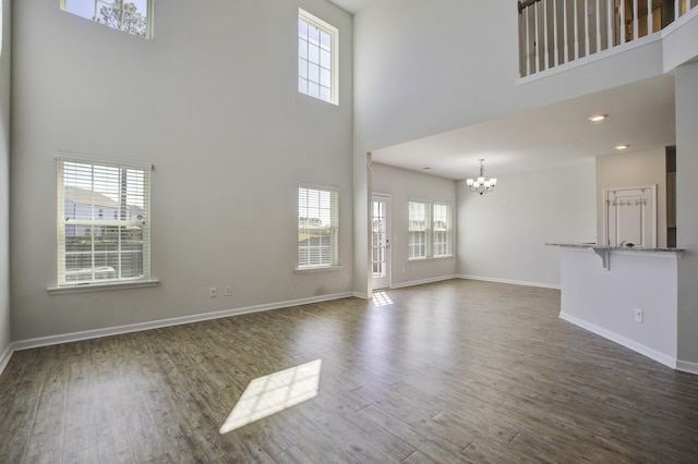 unfurnished living room with a notable chandelier, plenty of natural light, baseboards, and dark wood-style flooring