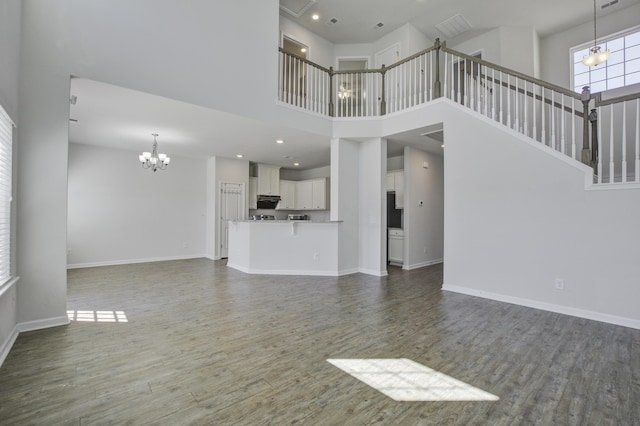 unfurnished living room featuring baseboards, dark wood-type flooring, a notable chandelier, and stairs