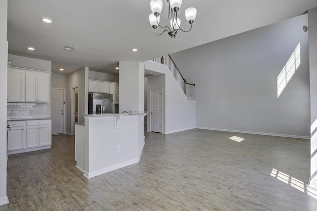 interior space with light stone counters, light wood-style flooring, white cabinetry, stainless steel fridge, and backsplash