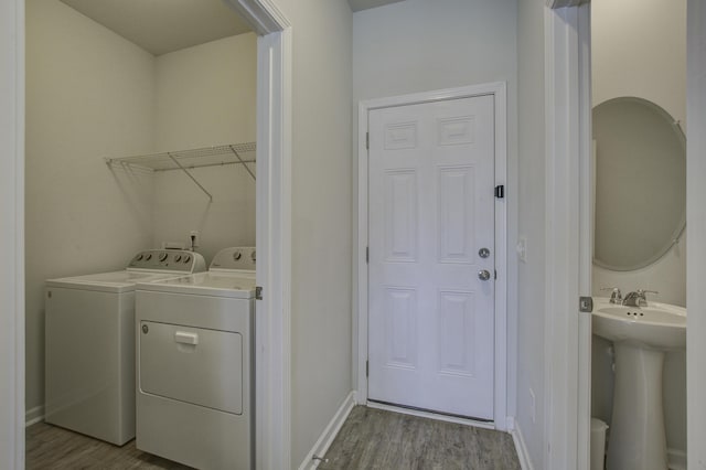 washroom featuring wood finished floors, baseboards, laundry area, a sink, and independent washer and dryer