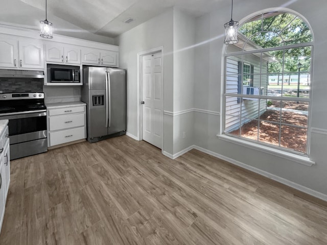 kitchen featuring decorative light fixtures, white cabinets, stainless steel appliances, and lofted ceiling