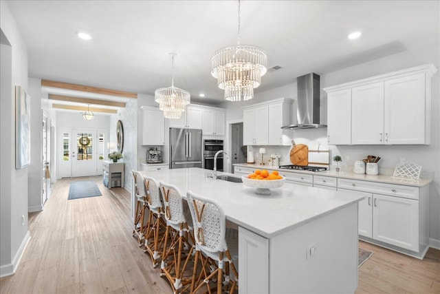 kitchen featuring a center island with sink, appliances with stainless steel finishes, wall chimney range hood, and white cabinets