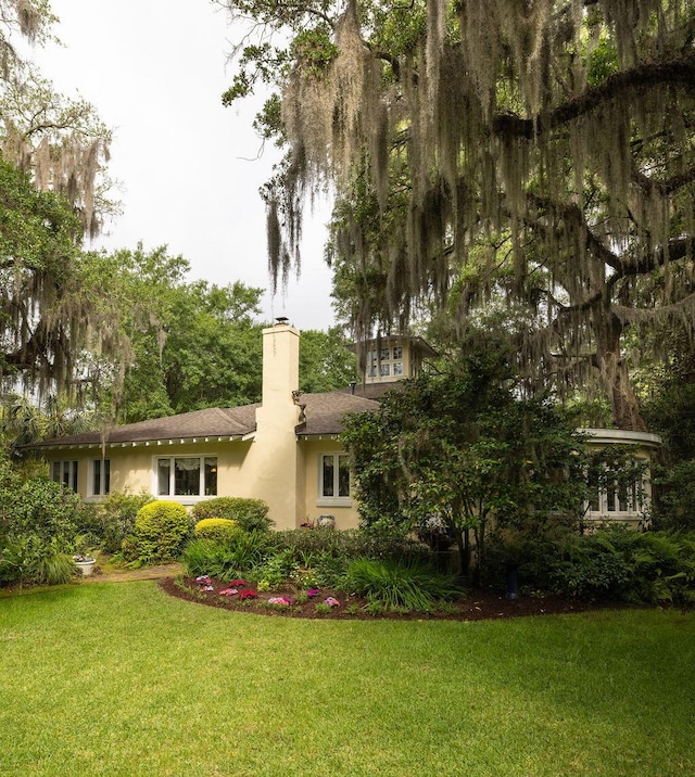 rear view of house with a chimney, a lawn, and stucco siding