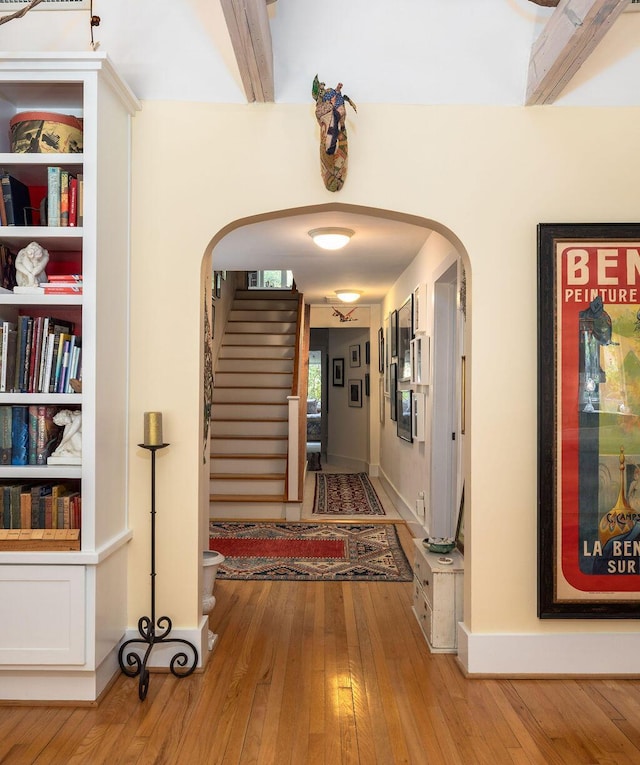 hallway featuring arched walkways, light wood-style flooring, stairway, and baseboards