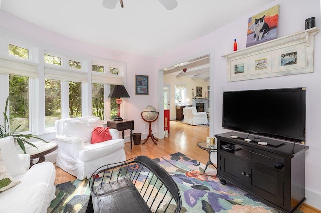 living area with a ceiling fan, wood finished floors, beamed ceiling, and baseboards