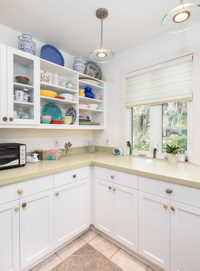 kitchen with white cabinets, light countertops, hanging light fixtures, and glass insert cabinets