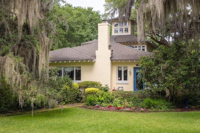 rear view of property featuring roof with shingles, a chimney, a yard, and stucco siding