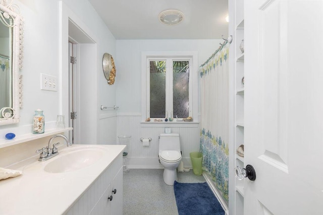 full bath with toilet, a wainscoted wall, and vanity
