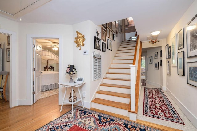 stairs with attic access, wood finished floors, a ceiling fan, and baseboards