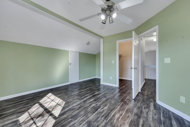 unfurnished bedroom with dark wood-type flooring, lofted ceiling, a walk in closet, a closet, and ceiling fan