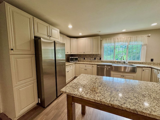 kitchen featuring stainless steel appliances, backsplash, light stone countertops, light hardwood / wood-style flooring, and sink