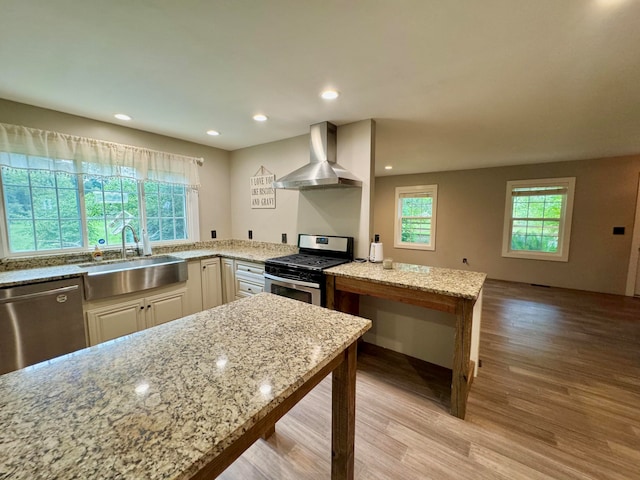 kitchen featuring light hardwood / wood-style flooring, light stone counters, plenty of natural light, wall chimney exhaust hood, and stainless steel appliances