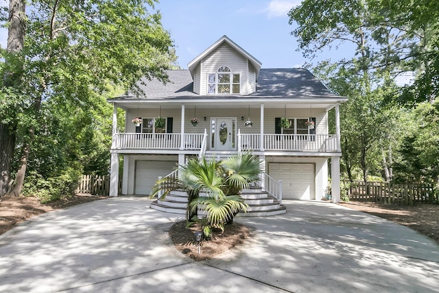 beach home featuring a garage, concrete driveway, a porch, and fence