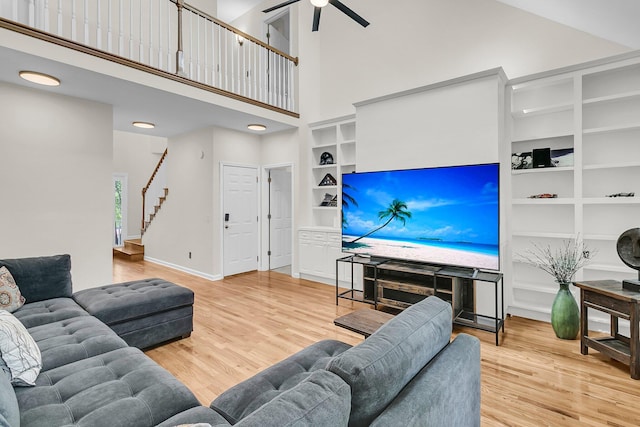 living room with a high ceiling, wood finished floors, a ceiling fan, stairs, and built in shelves