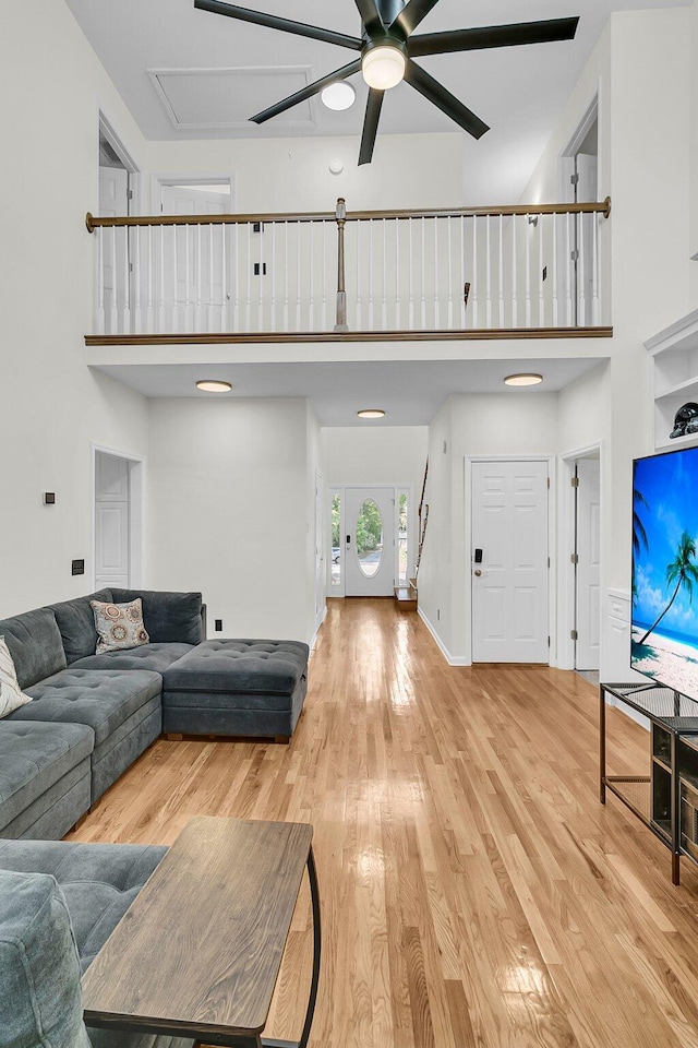 living area with a ceiling fan, a high ceiling, wood finished floors, and attic access