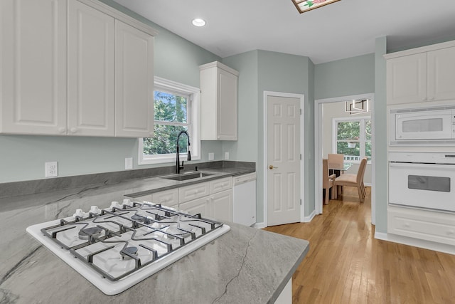 kitchen featuring white appliances, a sink, white cabinets, light wood-style floors, and recessed lighting