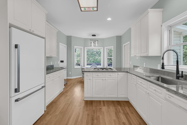 kitchen featuring white appliances, a sink, a peninsula, light wood-type flooring, and white cabinets