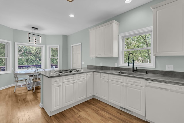 kitchen featuring white dishwasher, a sink, a peninsula, dark countertops, and recessed lighting