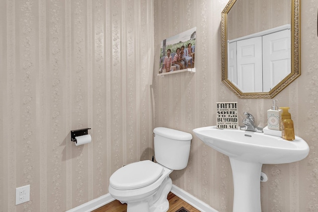 bathroom with wood finished floors, toilet, wallpapered walls, and baseboards