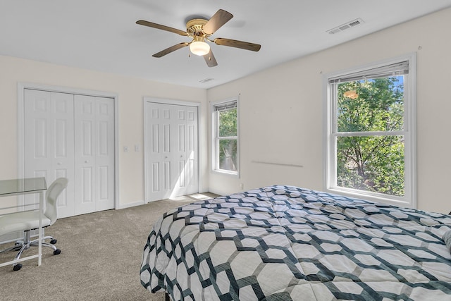 carpeted bedroom with two closets, ceiling fan, and baseboards