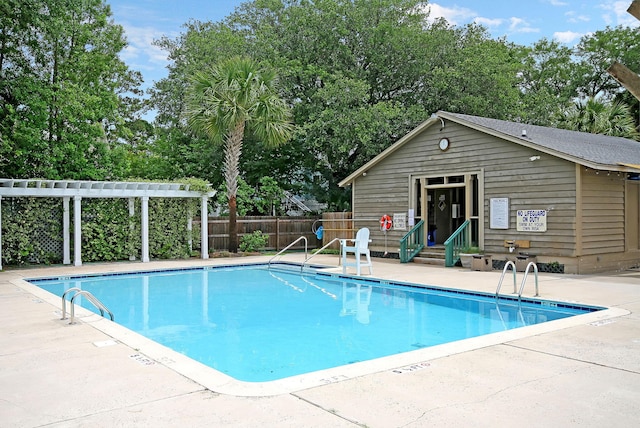 community pool featuring fence, an outdoor structure, a patio, and view of scattered trees