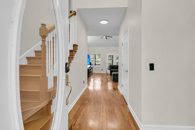 hall featuring light wood-style floors, stairs, and baseboards