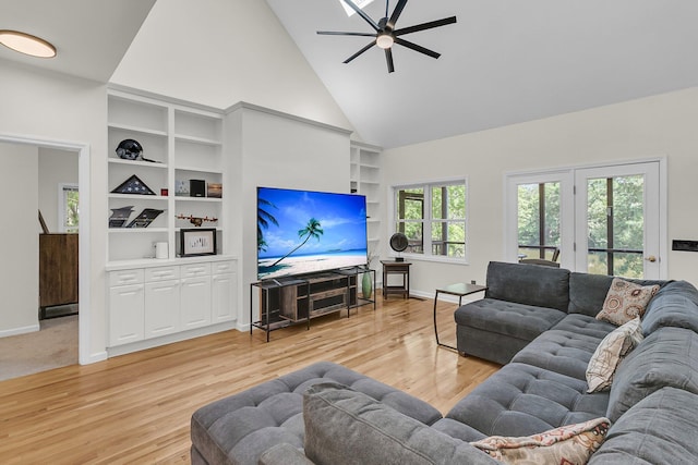 living room with a ceiling fan, built in features, light wood finished floors, baseboards, and high vaulted ceiling