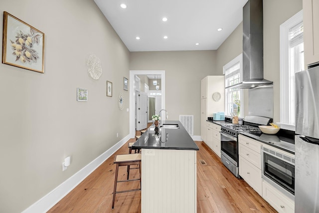 68 Vanderhorst St Unit A, Charleston, SC 29403 - kitchen featuring stainless steel appliances, wall chimney range hood, dark countertops, a breakfast bar area, and light wood-type flooring