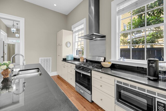 68 Vanderhorst St Unit A, Charleston, SC 29403 - kitchen featuring wall chimney range hood, stainless steel range with gas stovetop, dark countertops, built in microwave, and light wood-style floors